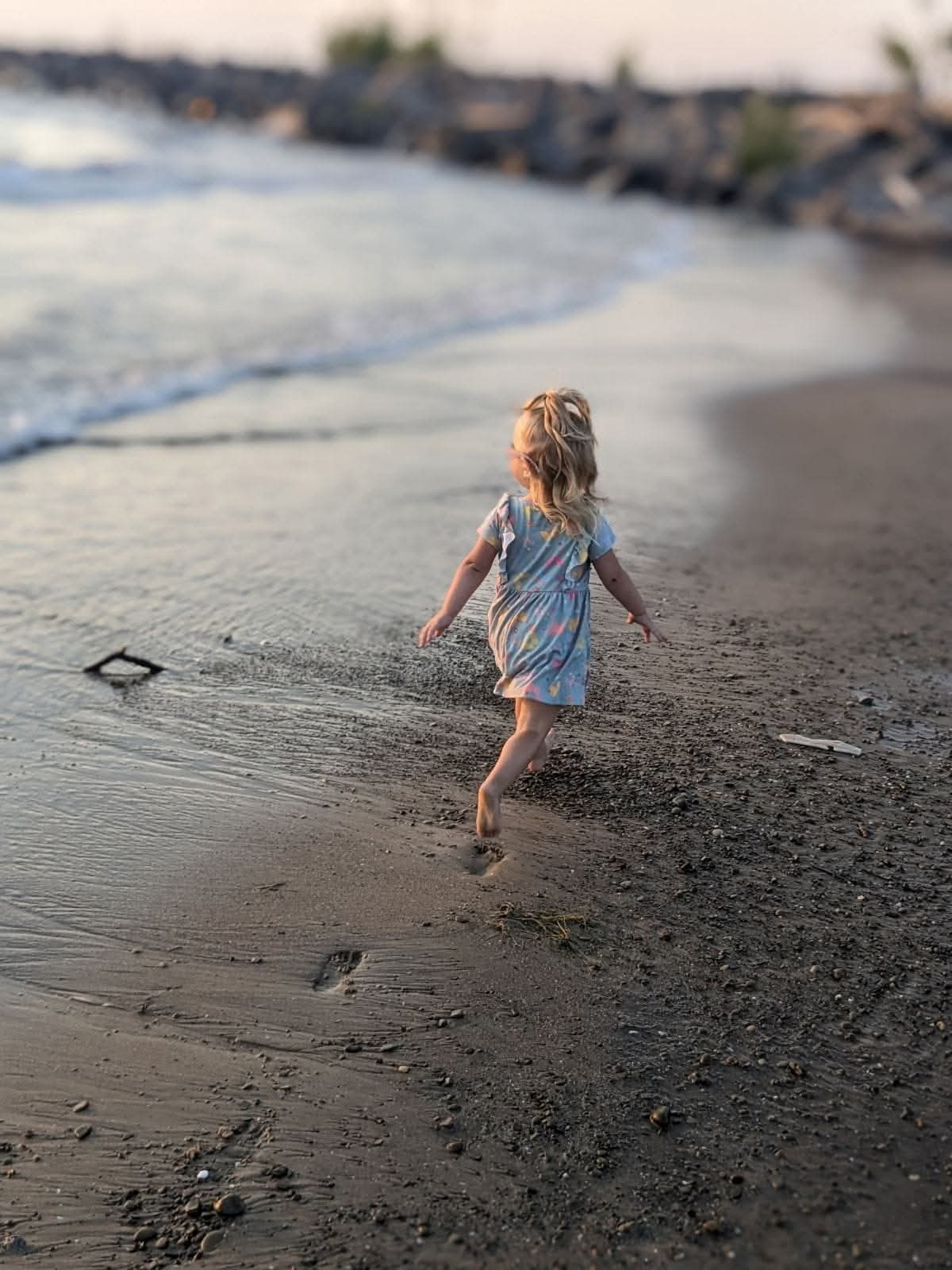 A young girl running barefoot along the shoreline at golden hour